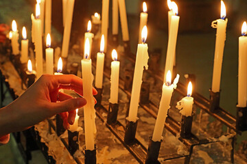 hand of girl that holding a lit candle in a church amidst a sea of flickering flames from the...