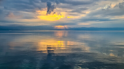 The sun setting behind mountains in Croatia. The Mediterranean Sea is calm and clear, reflecting...