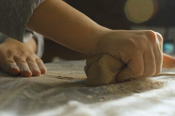 Women's hands knead dense clay for working on a potter's wheel.