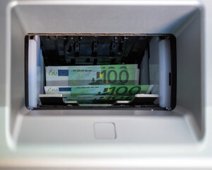 a lot of banknotes with a face value of one hundred euros are in the ATM tray