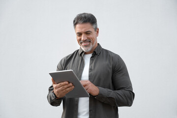 Succesful portrait of Hispanic mature adult professional business man working online. Smiling Indian senior businessman CEO holding digital tablet using tab application on isolated white background