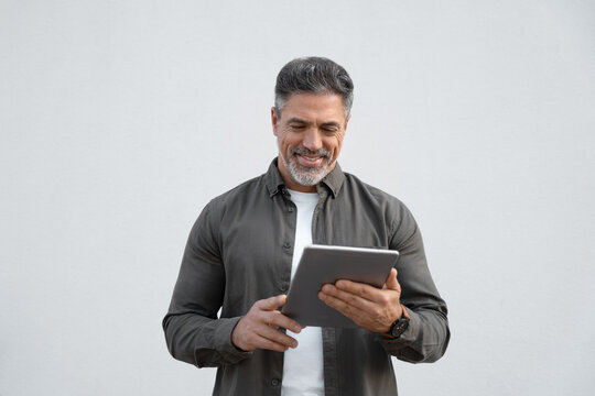 Happy Latin Hispanic bearded stylish mature adult professional business man, smiling Indian senior businessman CEO holding digital tablet using tab application standing on isolated white background