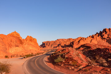 Panoramic sunrise view of endless winding empty road in Valley of Fire State Park leading to red Aztec Sandstone Rock formations and desert vegetation in Mojave desert, Overton, Nevada, USA. Freedom