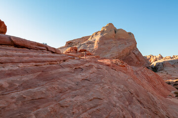 Woman with scenic sunrise view of arid landscape with striated red and white rock formations along the White Domes Hiking Trail in Valley of Fire State Park in Mojave desert, Overton, Nevada, USA