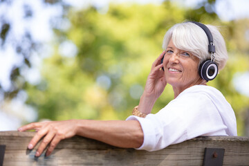 mature woman sat on park bench listening to headphones