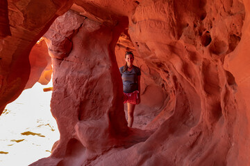 Woman standing in the fire cave and Windstone Arch in Valley of Fire State Park, Nevada, USA. Long, narrow slot canyon with sheer rock walls. Tranquil desert landscape of eroded sandstone formation © Chris