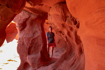 Woman standing in the fire cave and Windstone Arch in Valley of Fire State Park, Nevada, USA. Long, narrow slot canyon with sheer rock walls. Tranquil desert landscape of eroded sandstone formation © Chris