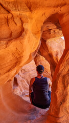 Man sitting in the fire cave and Windstone Arch in Valley of Fire State Park, Nevada, USA. Long, narrow slot canyon with sheer rock walls. Tranquil desert landscape of eroded sandstone formation