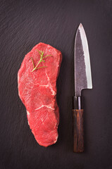 Raw dry aged angus roast beef steak offered as top view  on a design board with a Japanese santoku...