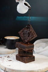 A decadent stack of rich chocolate brownies with smooth melted chocolate dripping from a cup onto...