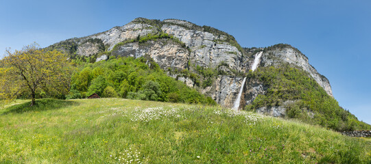 Large panorama of the Seerenbach Falls in spring with a green meadow and a blue sky