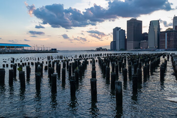 Fototapeta premium A pier on Hudson River in Brooklyn with the view on financial quarter of New York City. The sky is painted with soft colors of sunset. High skyscrapers reflecting on the water. Modern city.