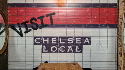 A metro station wall with the name of it on it - Chelsea Local. The wall is tilled blue, red and...