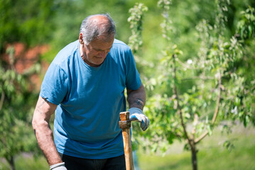 An elderly man is fixing his gardening tool. He is using suitable tools to fix his broken gardening...