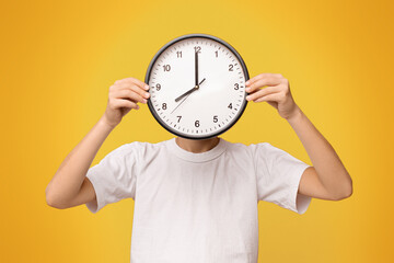 Teen boy covering his face with big clock, orange panorama