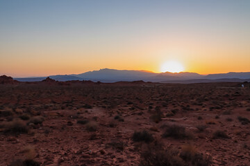 Fototapeta premium Sunrise over barren hills seen from Valley of Fire State Park in Mojave desert near Overton, Nevada, USA. Red rocks and stone desert. First sunlight with early morning atmosphere in remote habitat