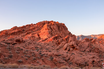 Panoramic sunrise view of red and orange Aztec Sandstone Rock formations and desert vegetation in Valley of Fire State Park in the Mojave desert near Overton, Nevada, USA. Dramatic natural landscape