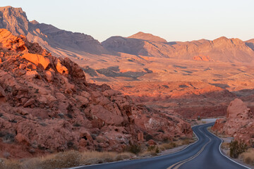 Panoramic sunrise view of endless winding empty road in Valley of Fire State Park leading to red...