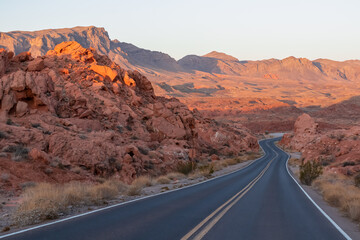Panoramic sunrise view of endless winding empty road in Valley of Fire State Park leading to red Aztec Sandstone Rock formations and desert vegetation in Mojave desert, Overton, Nevada, USA. Freedom
