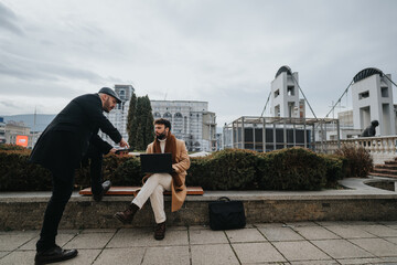 Outdoor business meeting with two professionals discussing over laptop in urban setting.