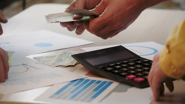 Family budget meeting, people count finances at table. Family budget planning, members tally at table. Table meeting for family budget, counting finances together. Teamwork on use of financial assets