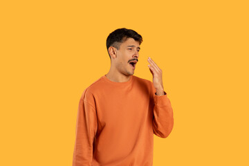 Young Man in Orange Sweatshirt Yawning Against Bright Yellow Background