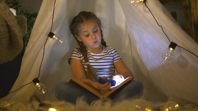 Child in tent with lantern reads book,embodying childhood dream.Lantern light illuminates pages, making every word part of childhood dream. irl plays and dreams of traveling with a tent. child at home