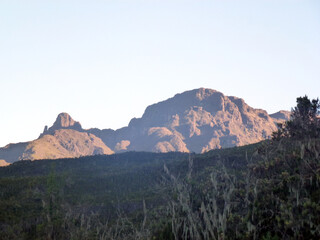 A picturesque view of a mountain valley overgrown with brown grass. Above it is a bright cloudless sky