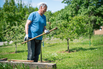 An elderly man is fixing his gardening tool. He is using suitable tools to fix his broken gardening tool. 
He is using his gardening tools for spring work in the orchard and wineyard.
