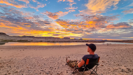 Man sitting on camping chair at Lone Rock beach campground with scenic sunrise view of Wahweap Bay...