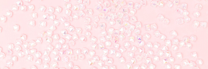 Banner with texture made from shiny iridescent beads scattered on a pink background.