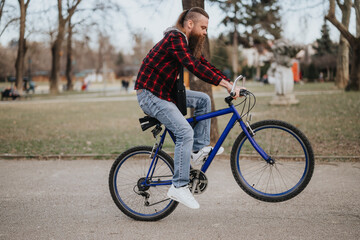Fototapeta premium Outdoor lifestyle capture of a man with a beard riding a blue bicycle in a public park, enjoying leisure time.