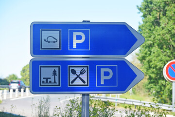 Panneau de signalisation sur une aire d'autoroute : parking pour voitures électriques, aire de pique-nique, restaurant.
