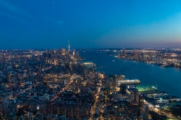 Fototapeta premium Captivating aerial view of New York's skyline and Hudson River right after the sunset seen from The Edge. The city is lit up by neon lights. Endless rows of buildings. Bustling city. Endless horizon