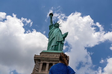 A woman in blue dress standing under an iconic representation of freedom and independence, the...