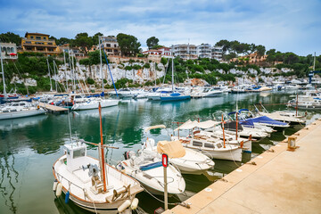 A serene view of the Porto Cristo harbor in Mallorca, showcasing moored boats and the surrounding...