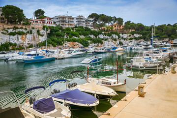 Fototapeta premium Amidst the tranquility of Porto Cristo harbor in Mallorca, moored boats adorn the waters, framed by the coastal beauty