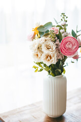 A lively bouquet of flowers arranged in a ribbed white vase showcases a kaleidoscope of colors and varieties, set on a wooden table near the window