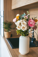 A gorgeous bouquet of assorted flowers in a white vase, positioned on the countertop of a stylish kitchen
