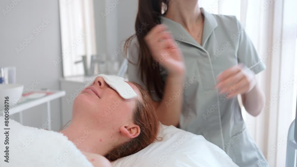 Wall mural Professional cosmetologist in uniform using LED mask on female patient for aesthetic treatment, relaxation, rejuvenation, color therapy, light therapy, skin care in beauty clinic.