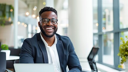 Naklejka premium Handsome African American man laughing joyfully at his office desk with laptop present