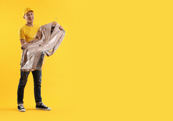 Dry-cleaning delivery. Happy courier holding coat in plastic bag on orange background, space for...
