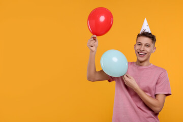 Happy man in party hat with balloons on orange background. Space for text