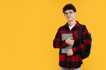 Portrait of student with backpack, laptop and glasses on orange background. Space for text