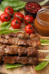 Tasty cooked marinated meat served with sauce and tomatoes on wooden table, closeup