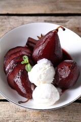 Tasty red wine poached pears and ice cream in bowl on wooden table, above view