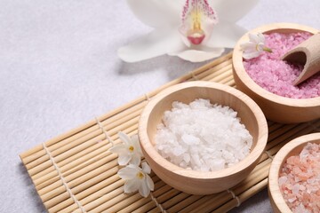 Different types of sea salt and flowers on light table, closeup. Spa products
