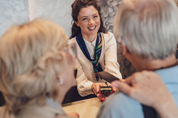 A senior couple at the hotel front desk makes contactless payments with a smartphone. Seniors...