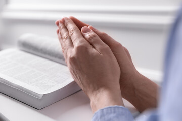 Religion. Christian woman praying over Bible indoors, closeup