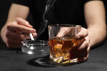 Alcohol addiction. Man with glass of whiskey and smoldering cigarette at dark textured table,...